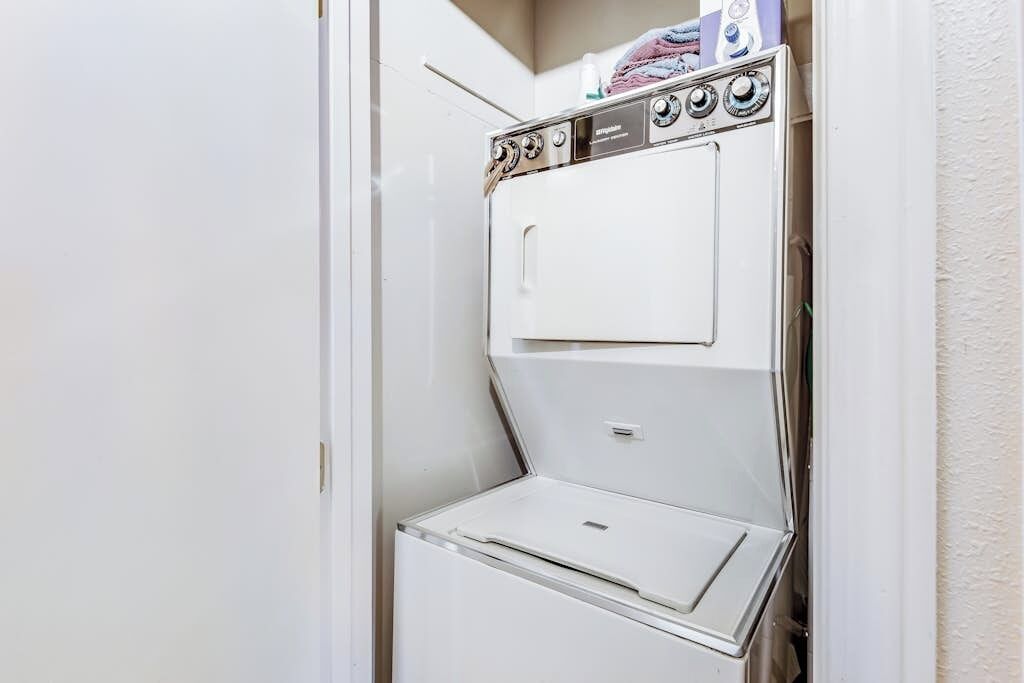 A white, wall-mounted, two-door washer and dryer unit with control knobs and a small shelf on top.