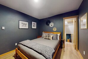Ein Schlafzimmer mit einem Bett, einem Nachttisch, einer Lampe und einer Tür zu einem anderen Raum.