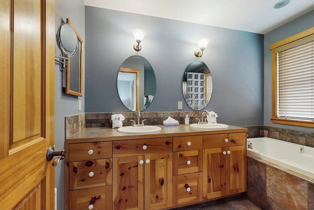 Ein Badezimmer mit einem Holzbadschrank, zwei Waschbecken, einem Spiegel und einer Badewanne.