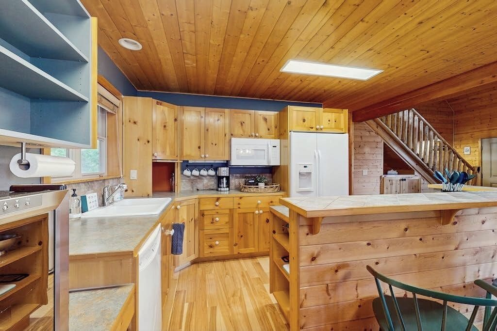 A wooden cabin interior with a kitchen area, wooden cabinets, a microwave, a refrigerator, and a staircase leading to another level.