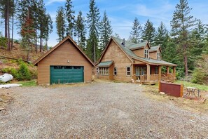 A two-story wooden cabin with a covered porch and a gravel driveway. - 3BR Cabin, dog-friendly with fireplace and views (Cle Elum)