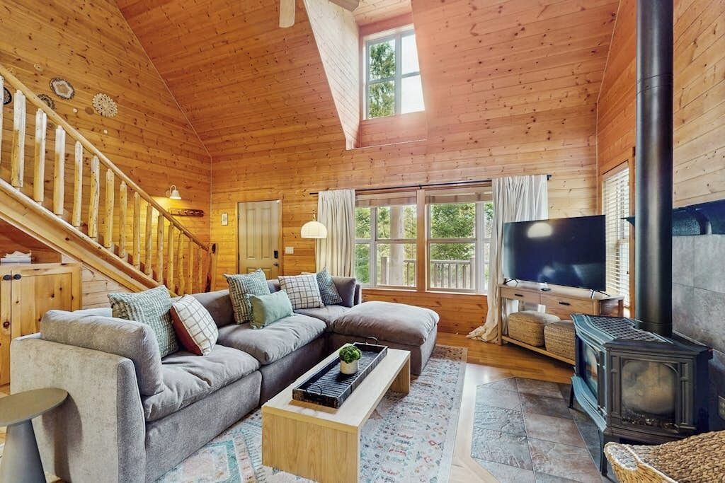 Ein gemütliches Blockhauss Innenleben mit einer Holztreppe, einem Ecksofa, einem Fernseher und einem Kaminofen.