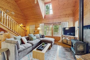 A cozy cabin interior with a wooden staircase, a sectional sofa, a television, and a wood-burning stove. - 3BR Cabin, dog-friendly with fireplace and views (Cle Elum)