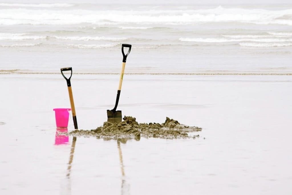 Two shovels on a beach with a pink bucket.