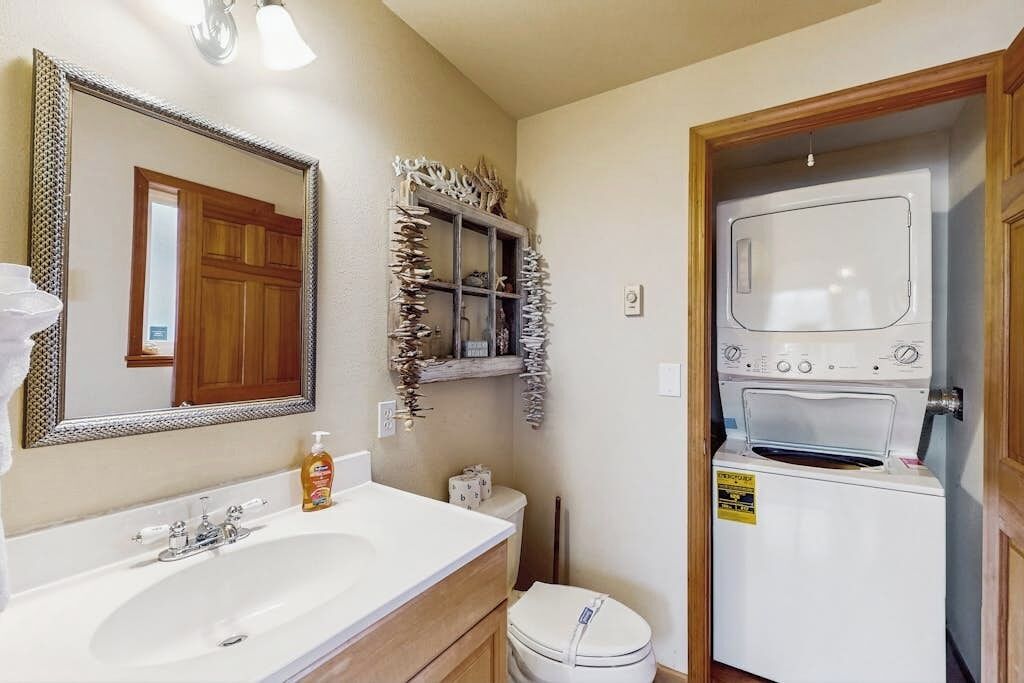 A bathroom with a sink, mirror, toilet, and a washing machine.