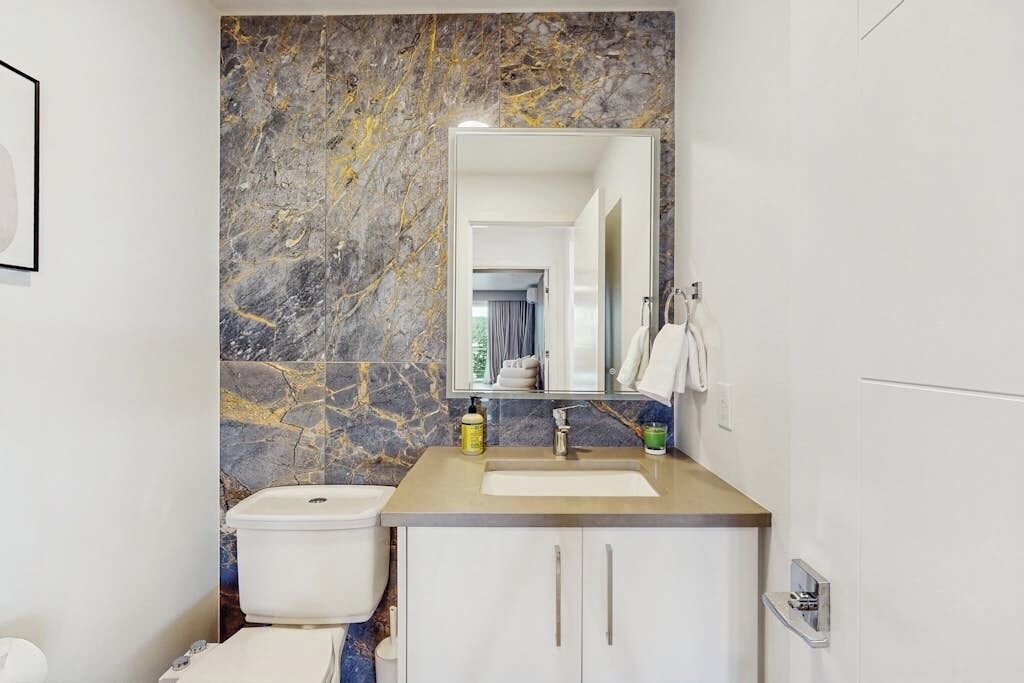 A bathroom with a marble wall, a sink, a toilet, and a mirror.