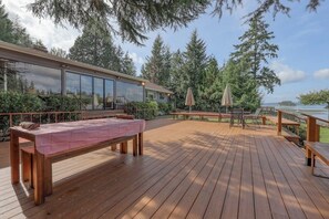 A wooden deck with a checkered table, outdoor seating, and a view of a lake. - Large 4BR Bayview Dog Friendly - Deck - Firepit (Gig Harbor)
