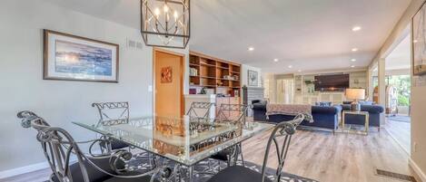 A dining area with a glass table and metal chairs, a bookshelf, and a sofa in the background.