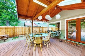 An outdoor deck with a wooden table and chairs, a wooden fence, and a view of a house in the background. - 3BR dog-friendly riverfront home with patio, golf (Renton)
