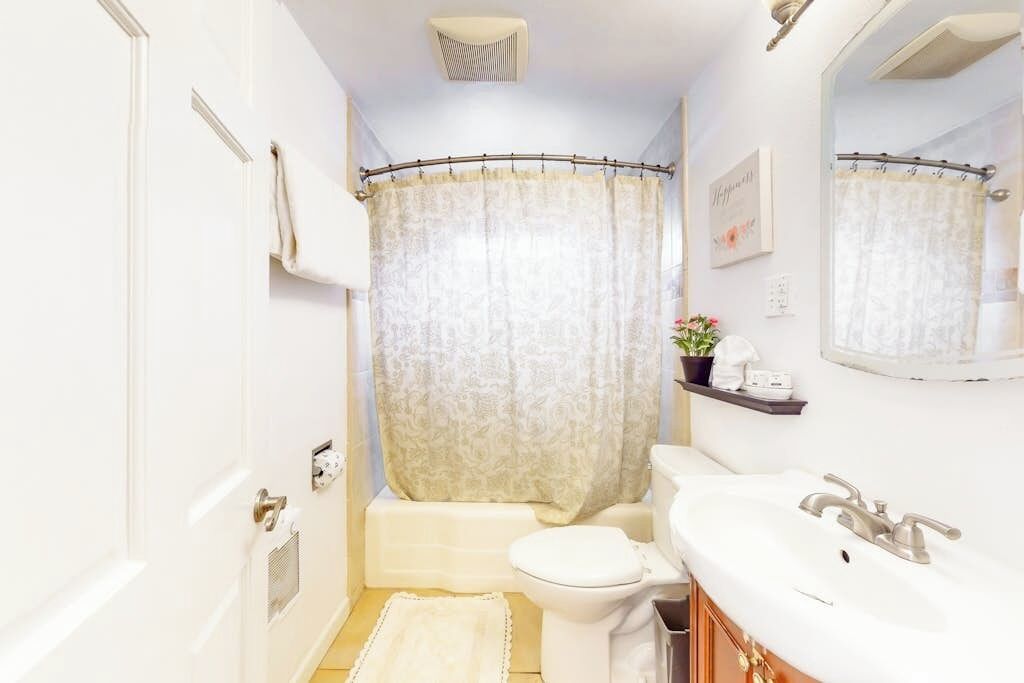 A bathroom with a toilet, sink, shower curtain, and a small shelf with toiletries.