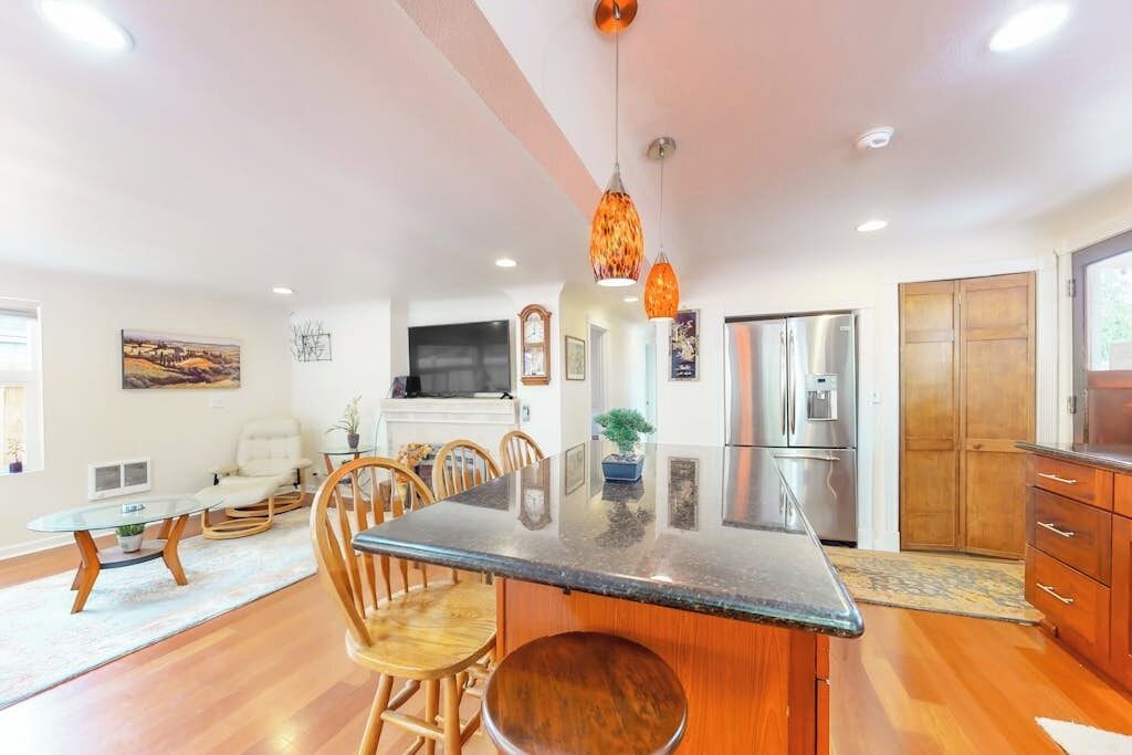 A modern kitchen with a central island, wooden chairs, and pendant lighting.