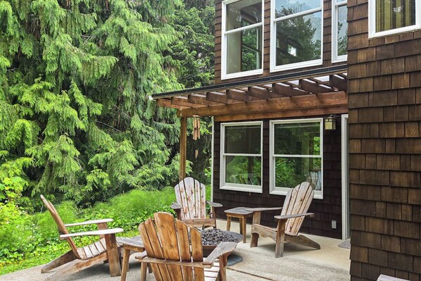 Ein Holzhaus mit überdachter Terrasse, Sitzgelegenheiten im Freien und Wald im Hintergrund.