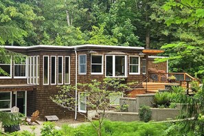 Ein modernes, zweistöckiges Haus mit großen Fenstern, einer Terrasse und einer Treppe zu einer Veranda.