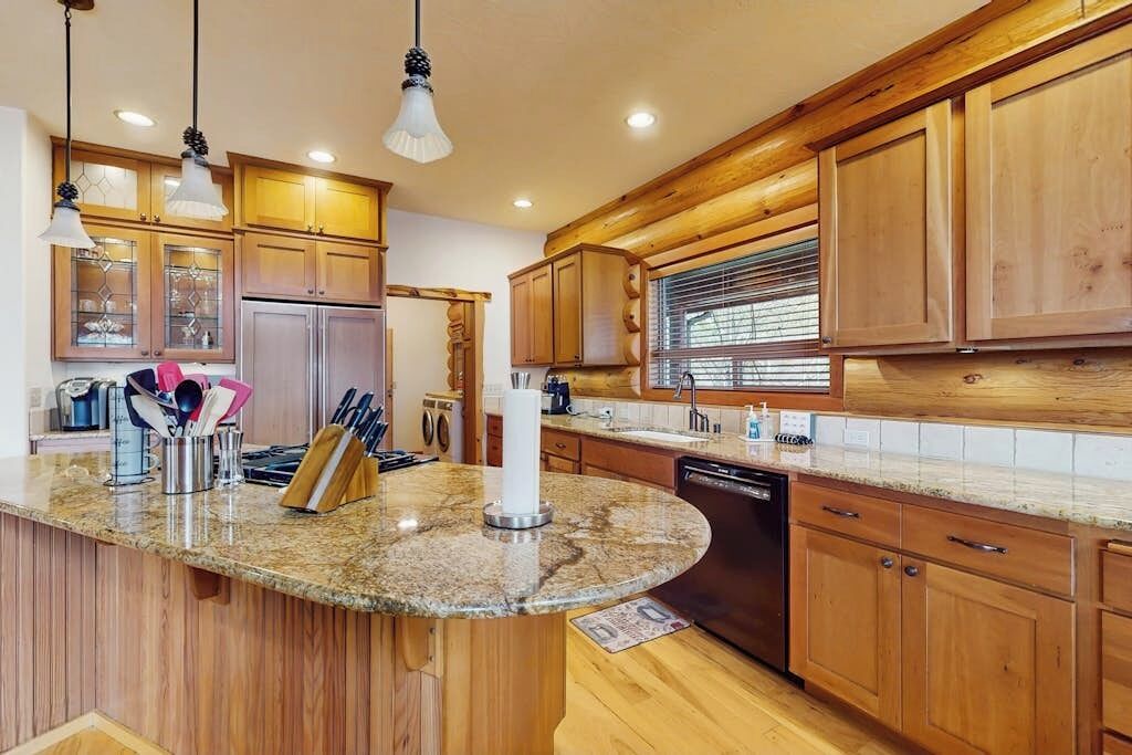 A kitchen with wooden cabinets, granite countertops, a dishwasher, and hanging pendant lights.