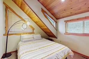 A bedroom with a sloped ceiling, a bed with striped bedding, a floor lamp, and a window with blinds. - 3BR lakefront home with game room and kayaks (Olympia)