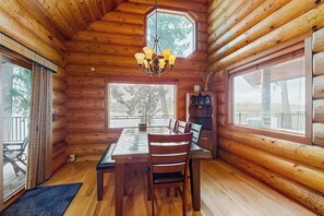 A log cabin interior with a dining table, chairs, a chandelier, and large windows. - 3BR lakefront home with game room and kayaks (Olympia)