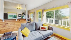 A modern living room with a grey sofa, yellow cushions, and a view of a balcony. - 3BR water view home, pet and family friendly (Raymond)