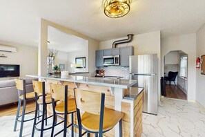 Una cocina moderna con una isla central, taburetes de bar y una zona de comedor con sofá.