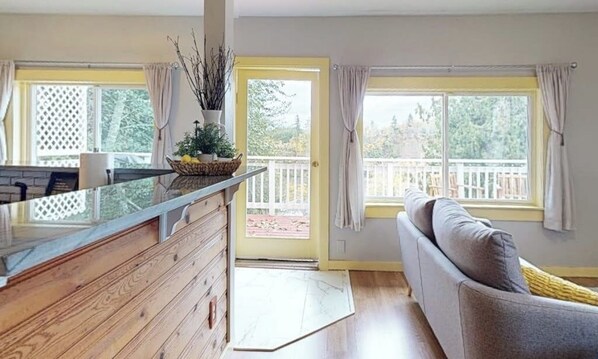 Una sala de estar con un sofá, una mesa de centro de vidrio y vistas al exterior por una puerta corrediza.