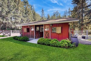 A red barn with a covered entrance, surrounded by a fenced area and lush greenery. - 0BR Studio on lush grounds with nearby horses (Bainbridge Island)