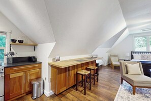 A loft-style room with a kitchen area, a dining bar, and a seating area with a sofa and chairs. - 0BR Studio on lush grounds with nearby horses (Bainbridge Island)