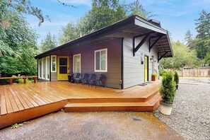 A single-story house with a wooden deck, a covered porch, and a small garden area. - 4BR Home with bright open living (Bainbridge Island)
