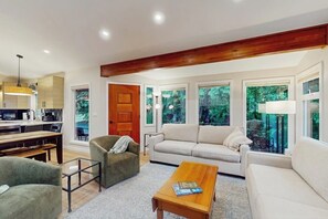 A modern living room with a sofa, armchair, coffee table, and dining area. - 4BR Home with bright open living (Bainbridge Island)