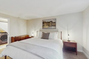 A bedroom with a large bed, a painting on the wall, a nightstand, and a washing machine in the corner. - 4BR Home with bright open living (Bainbridge Island)