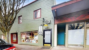 En byggnad med en skylt som visar att det är ett hotell, en butiksfasad med olika varor till försäljning och ett träd framför.