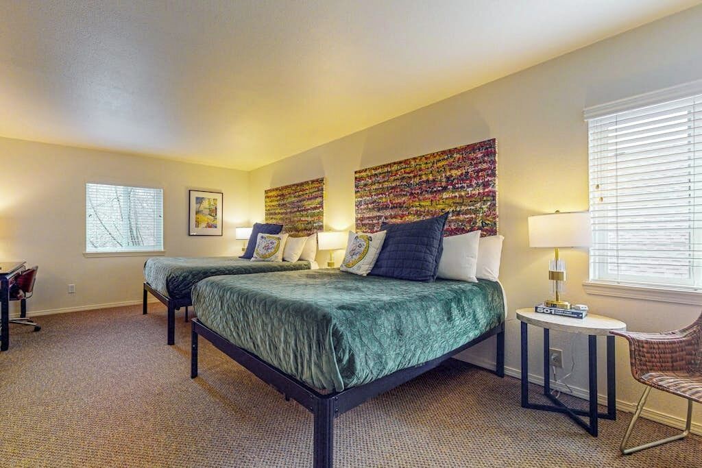 A hotel room with two beds, a desk, a chair, and a large window.