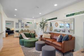 A modern living room with a green sectional sofa, a brown leather couch, and a large mirror. - 3BR waterfront home with patio & wildlife watching (Lilliwaup)