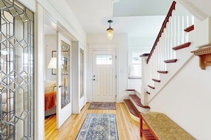A hallway with a wooden floor, a patterned rug, a bench, a door, and a staircase with wooden railings. - Waterfront house with beach access (Kingston)