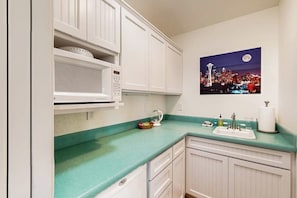 A kitchen with white cabinets, a green countertop, a microwave, a sink, and a cityscape painting on the wall. - Waterfront house with beach access (Kingston)