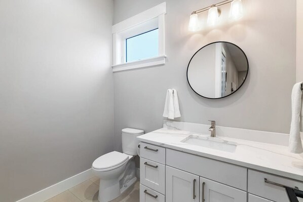 A bathroom with a toilet, a sink, a mirror, and a window. - 3BR dog friendly getaway with a game room (Westport)