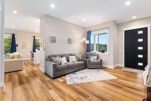 A spacious living room with a grey sofa set, a coffee table, and a large window with curtains.