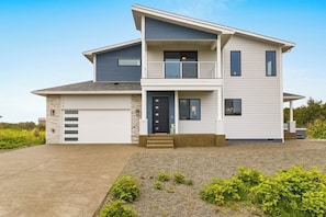 A two-story modern house with a garage, a front porch, and a small garden area.