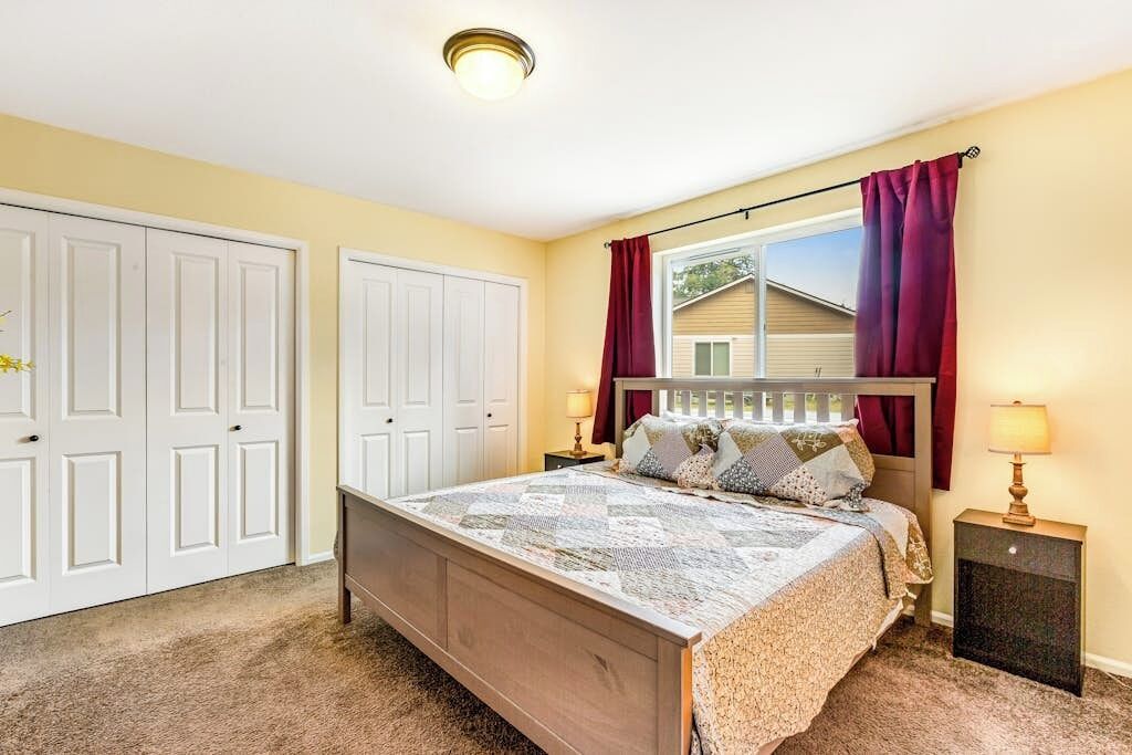 Une chambre à coucher avec un lit, deux tables de chevet, une fenêtre avec des rideaux et une porte.
