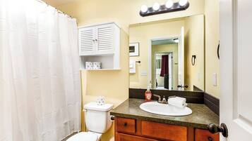 A bathroom with a toilet, sink, vanity, and a shower curtain.