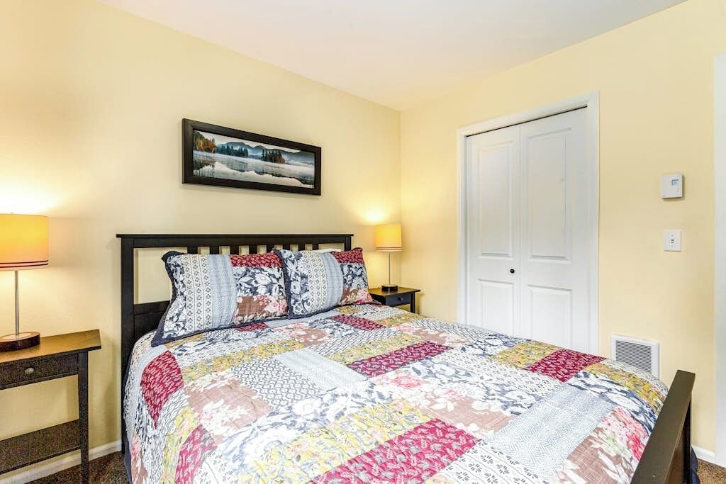 A bedroom with a bed, two bedside tables, a nightstand, a door, and a wall-mounted picture.