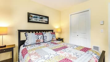 A bedroom with a bed, two bedside tables, a nightstand, a door, and a wall-mounted picture.