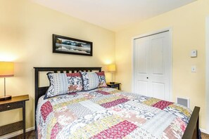 A bedroom with a bed, two bedside tables, a nightstand, a door, and a wall-mounted picture.