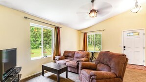 Ein Wohnzimmer mit einer Sofagarnitur, einem Couchtisch, einem Flachbildfernseher und einem Deckenventilator.