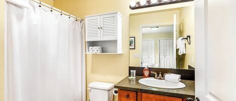 A bathroom with a toilet, a sink, a vanity with a mirror, and a shower curtain.