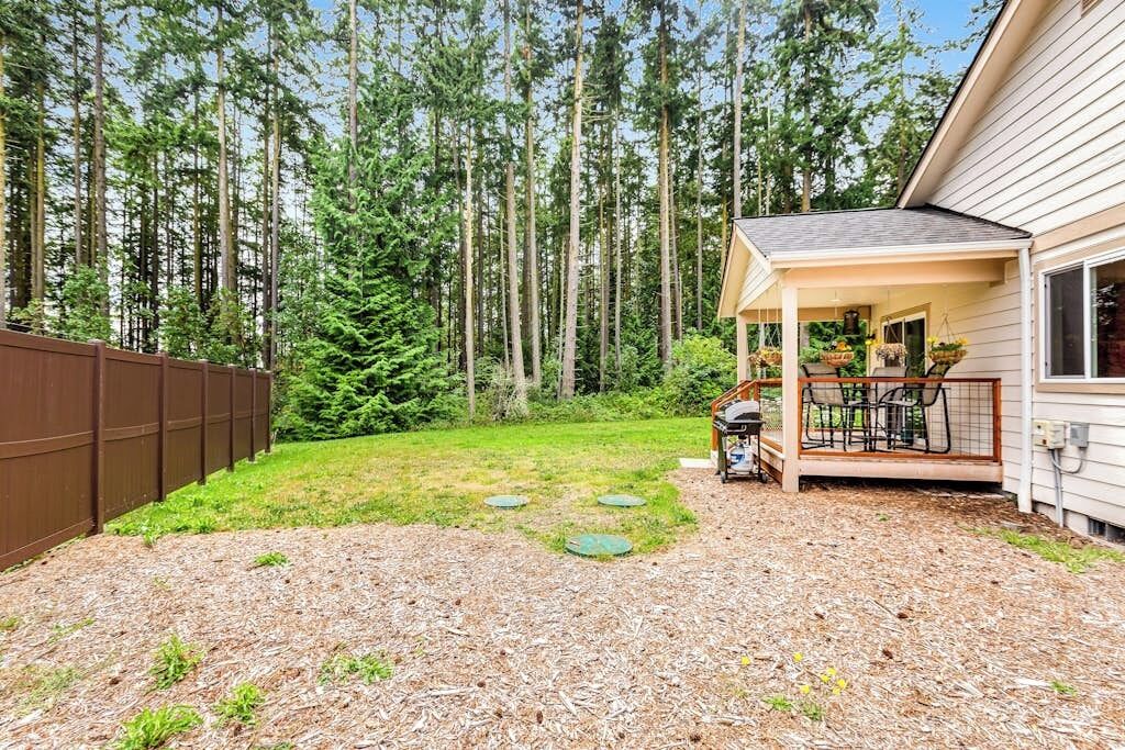 A residential backyard with a covered patio, a wooden fence, and a dense forest in the background.