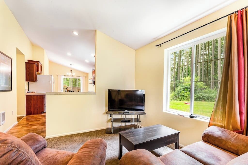 A living room with a television, sofa, and a window with curtains.