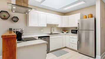 A modern kitchen with white cabinets, a stainless steel refrigerator, and a skylight.
