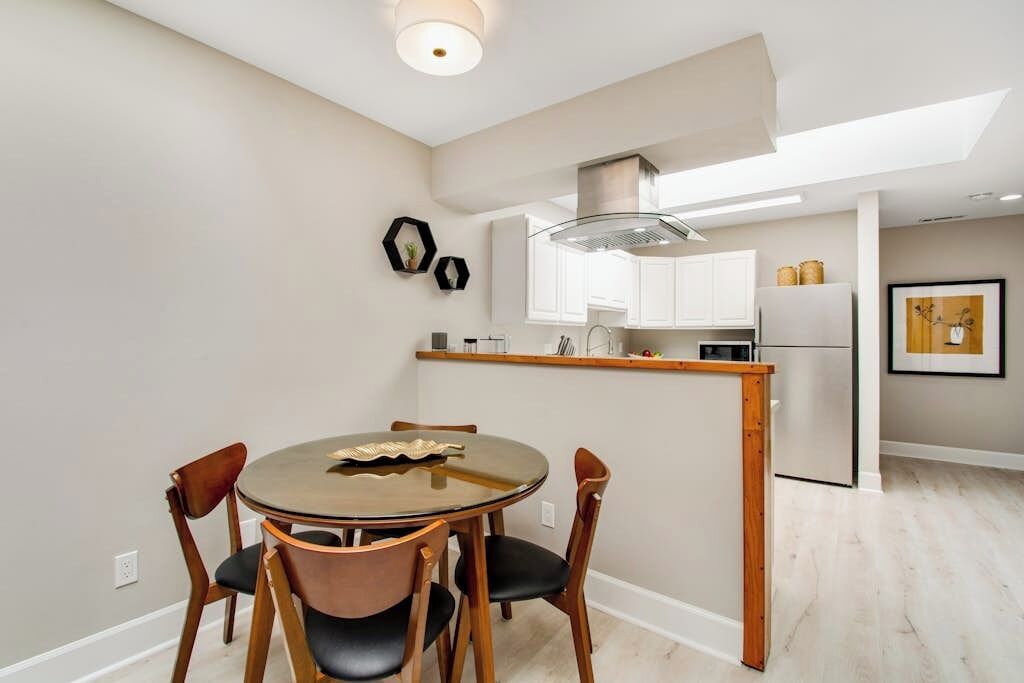 A modern kitchen with white cabinets, a stainless steel refrigerator, and a dining area with a round table and chairs.