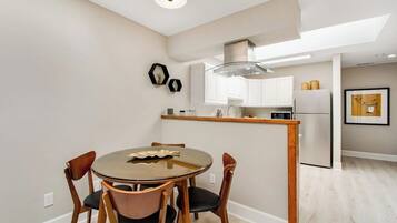 A modern kitchen with white cabinets, a stainless steel refrigerator, and a dining area with a round table and chairs.