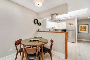 A modern kitchen with white cabinets, a stainless steel refrigerator, and a dining area with a round table and chairs.