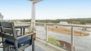 Een balkon met uitzicht op een weg en groen, een tafel met een stoel en een hekwerk.